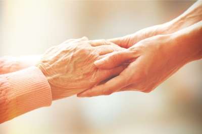 Des mains de personne agée soutenues par des mains de femme plus jeune.